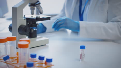 Close-Up-Of-Lab-Worker-Conducting-Research-Using-Microscope-Holding-Blood-Sample-Labelled-Type-O