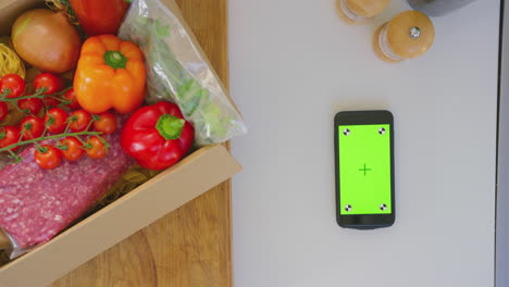 Overhead-shot-of-box-of-fresh-ingredients-next-to-green-screen-mobile-phone---shot-in-slow-motion