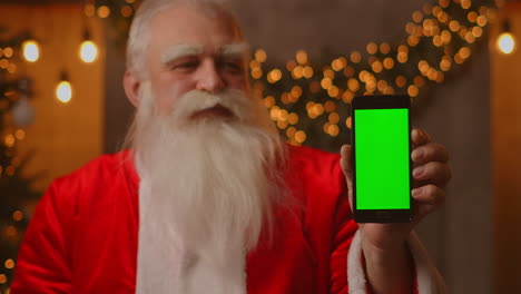 Santa-points-his-finger-at-the-green-screen-mobile-phone-screen.-Christmas-sale.-Elderly-Santa-Claus-shows-a-screen-with-a-chromakey.-High-quality-4k-footage