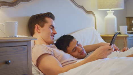 Liebendes-Gleichgeschlechtliches-Männliches-Paar,-Das-Zu-Hause-Im-Bett-Liegt-Und-Ein-Selfie-Des-Schlafenden-Partners-Mit-Dem-Mobiltelefon-Macht