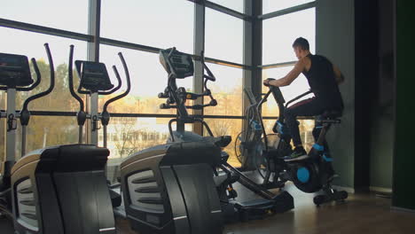 Young-active-men-spinning-a-air-bike-in-gym-with-trainers.-male-training-on-air-bike.