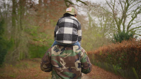 Rear-View-Of-Soldier-In-Uniform-Returning-Home-To-Family-On-Leave-Carrying-Son-Wearing-Army-Cap
