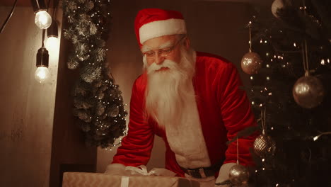Santa-Claus-brings-gifts-under-the-Christmas-tree-for-children.-Give-gifts-to-children-on-Christmas-night.-Santa-puts-a-gift-under-the-Christmas-tree.-High-quality-4k-footage