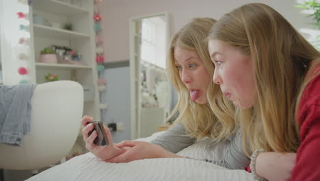 Mother-with-teenage-daughter-wearing-pyjamas-lying-on-bed-posing-for-selfie-on-mobile-phone---shot-in-slow-motion