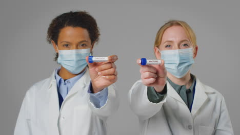 Studio-Shot-Of-Lab-Research-Workers-In-Face-Masks-Holding-Test-Tubes-Labelled-Omicron-And-Vaccine