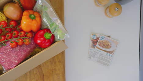 Overhead-shot-of-box-of-fresh-ingredients-next-to-recipe-cards-in-kitchen---shot-in-slow-motion