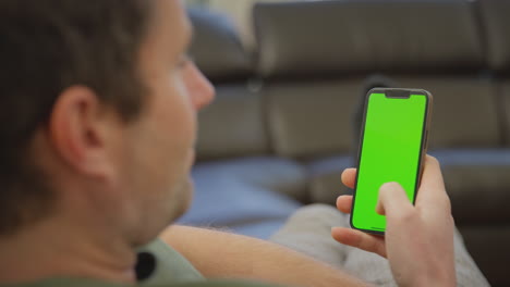 Close-up-of-man-wearing-pyjamas-lying-on-sofa-at-home-looking-at-green-screen-mobile-phone---shot-in-slow-motion