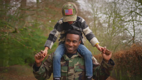 American-Soldier-In-Uniform-Returning-Home-To-Family-On-Leave-Carrying-Son-Wearing-Army-Cap