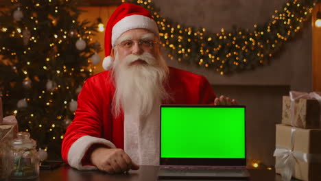 Santa-holds-a-laptop-with-a-green-screen-while-sitting-in-the-Christmas-decorations.-High-quality-4k-footage