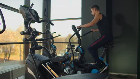 Fit-young-men-using-air-bike-at-the-gym.-Strong-male-athlete-doing-cardio-workout-on-cycle-at-health-club-on-big-windows