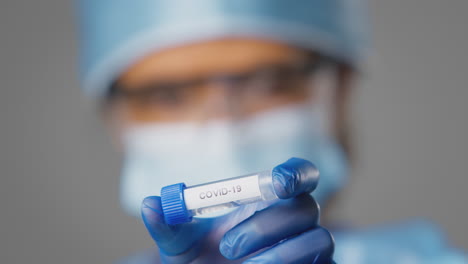 Close-Up-Of-Female-Lab-Research-Worker-Wearing-PPE-Holding-Test-Tube-Labelled-Covid-19