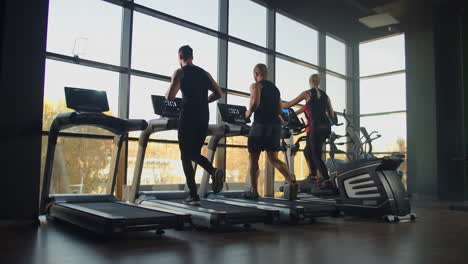 A-group-of-people-running-on-a-treadmill-in-a-fitness-room-performing-a-cardio-workout.-Men-and-women-train-together-Running-indoors-warm-up-before-training-in-slow-motion.