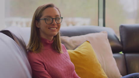 Portrait-Of-Smiling-Woman-Wearing-Glasses-Relaxing-On-Sofa-At-Home