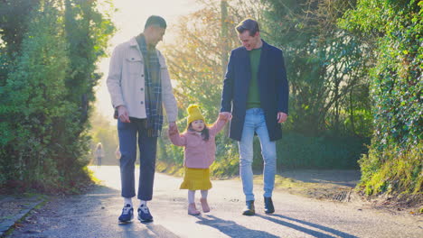 Close-Up-Of-Family-With-Two-Dads-Taking-Daughter-For-Walk-In-Fall-Or-Winter-Countryside