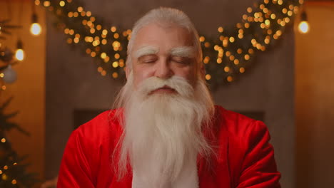 Headshot-Looking-at-the-camera-Happy-old-bearded-Santa-Claus-wearing-costume-and-waving-hand-video-calling-in-zoom-recording-video-Merry-Christmas-greeting-face-camera-view.-High-quality-4k-footage