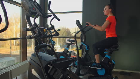 Young-active-woman-spinning-a-air-bike-in-gym-with-trainers.-Female-training-on-air-bike