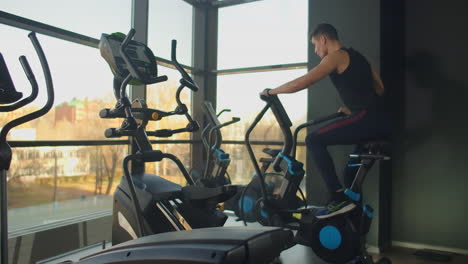 Young-active-men-spinning-a-air-bike-in-gym-with-trainers.-male-training-on-air-bike.