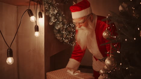 Santa-brings-a-gift-to-children-on-Christmas-night-and-puts-it-near-the-Christmas-tree-in-the-children-house.-the-camera-monitors-the-delivery-of-the-gift-under-the-tree.-High-quality-4k-footage