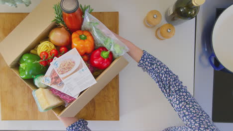 View-from-above-of-woman-with-recipe-cards-and-box-of-delivered-fresh-ingredients-planning-meal---shot-in-slow-motion