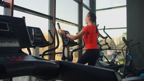 Beautiful-fit-sportive-positive-young-woman-in-gym-doing-exercises-on-elliptical-trainer-working-out.-Slow-motion-the-woman-on-the-elliptical-trainer.