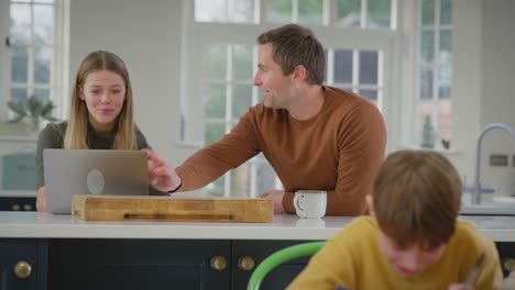 Parents-helping-son-and-teenage-daughter-with-homework-sitting-in-kitchen-at-home---shot-in-slow-motion