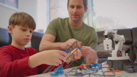 Father-and-son-wearing-pyjamas-building-robotic-arm-from-plastic-kit-at-home-for-science-project---shot-in-slow-motion