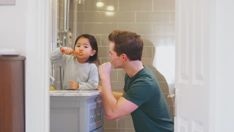Family-With-Dad-And-Daughter-Brushing-Teeth-In-Bathroom-At-Home-Together