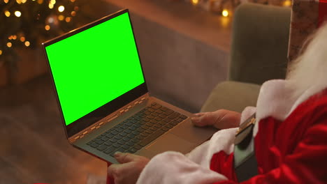 Während-Der-Quarantäne-Gratuliert-Der-Weihnachtsmann-Den-Kindern-Per-Videoschalte.-Grüner-Bildschirm-Des-Laptops-Auf-Dem-Schoß-Des-Weihnachtsmanns.-Rückansicht-Eines-Laptop-Bildschirms-Mit-Einem-Chromakey-Auf-Dem-Hintergrund-Eines-Weihnachtsbaums.-Hochwertiges-4K-Filmmaterial