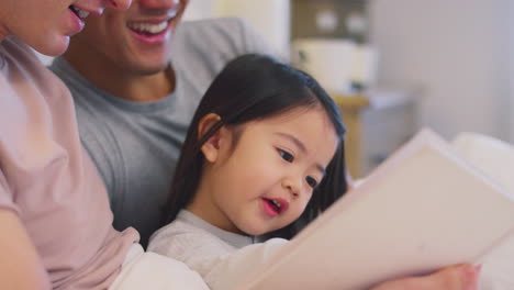 Family-With-Two-Fathers-In-Bed-At-Home-Reading-Story-To-Daughter