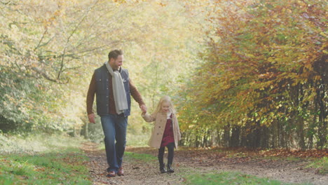 Father-And-Daughter-Holding-Hands-And-Skipping-On-Family-Walk-Along-Track-In-Autumn-Countryside