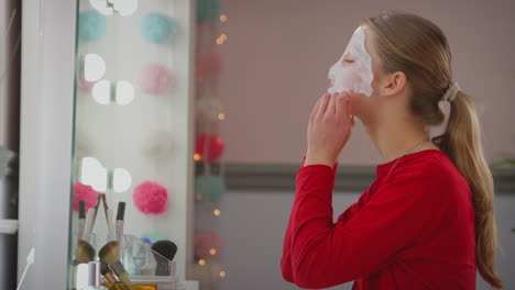 Teenage-girl-wearing-pyjamas-putting-on-face-mask-in-bedroom-mirror-at-home---shot-in-slow-motion