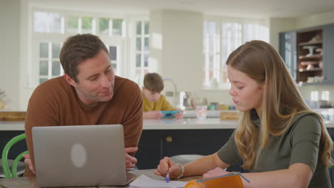 Eltern-Helfen-Ihrer-Tochter-Im-Teenageralter-Bei-Den-Hausaufgaben,-Indem-Sie-Zu-Hause-Am-Küchentisch-Sitzen-Und-Einen-Laptop-Benutzen-–-Aufgenommen-In-Zeitlupe