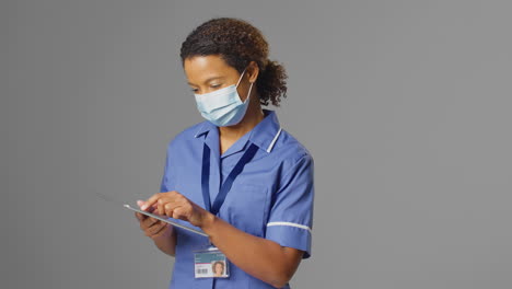 Retrato-De-Estudio-De-Una-Enfermera-Con-Uniforme-Y-Mascarilla-Usando-Una-Tableta-Digital