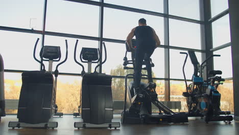 Back-view-a-man-in-the-cardio-area-of-the-gym-trains-on-an-elliptical-trainer.