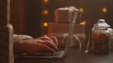 Hands-Santa-typing-on-wireless-keyboard-by-wooden-New-Year-decorated-table-Santa-Claus-is-working-with-a-laptop-looking-through-mail-and-answering-messages-to-children.-High-quality-4k-footage