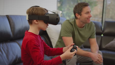Father-watching-son-wearing-virtual-reality-headset-play-computer-game-sitting-on-sofa-at-home---shot-in-slow-motion