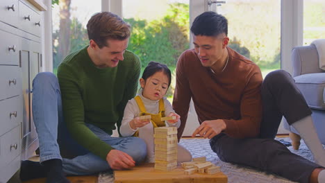 Familie-Mit-Zwei-Vätern-Spielt-Mit-Ihrer-Tochter-Zu-Hause-Und-Stapelt-Holzsteine-In-Einen-Turm