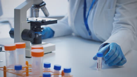 Close-Up-Of-Lab-Worker-Conducting-Research-Using-Microscope-Holding-Blood-Sample-Labelled-Type-AB