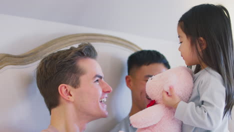 Family-With-Two-Dads-In-Bed-At-Home-Playing-Game-With-Daughter-And-Her-Soft-Toy