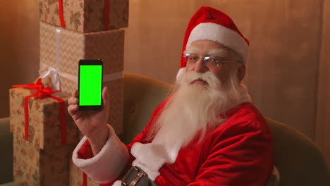 Der-Weihnachtsmann-Zeigt-Mit-Dem-Finger-Auf-Den-Grünen-Bildschirm-Des-Mobiltelefons.-Weihnachtsverkauf.-Der-ältere-Weihnachtsmann-Zeigt-Einen-Bildschirm-Mit-Einem-Chromakey.-Hochwertiges-4K-Filmmaterial