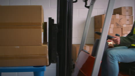 Female-Worker-With-Clipboard-In-Warehouse-Talking-To-Colleague-Driving-Fork-Lift-Truck