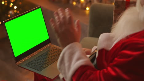 Während-Der-Quarantäne-Gratuliert-Der-Weihnachtsmann-Den-Kindern-Per-Videoschalte.-Grüner-Bildschirm-Des-Laptops-Auf-Dem-Schoß-Des-Weihnachtsmanns.-Rückansicht-Eines-Laptop-Bildschirms-Mit-Einem-Chromakey-Auf-Dem-Hintergrund-Eines-Weihnachtsbaums.-Hochwertiges-4K-Filmmaterial