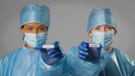 Studio-Shot-Of-Female-Lab-Research-Workers-In-PPE-Holding-Test-Tubes-Labelled-Omicron-And-Vaccine