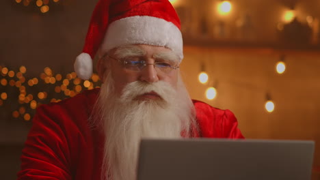 Weihnachtsmann-Benutzt-Laptop-Im-Wohnzimmer.-Porträt-Des-Nachdenklichen-Weihnachtsmanns,-Der-Mit-Modernem-Laptop-In-Dekoriertem-Haus-Tippt.-Hochwertiges-4K-Filmmaterial
