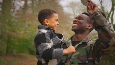 Close-Up-Of-American-Soldier-Returning-Home-To-Family-On-Leave-Carrying-Son-Wearing-Army-Cap