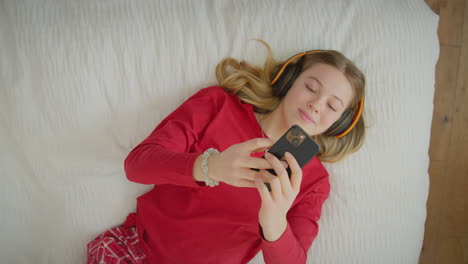 View-from-above-of-teenage-girl-wearing-wireless-headphones-streaming-music-or-film-from-mobile-phone---s-hot-in-slow-motion