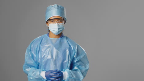 Portrait-Of-Serious-Female-Surgeon-Wearing-Safety-Glasses-And-Face-Mask-Against-Grey-Background