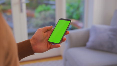 Close-Up-Of-Man-At-Home-Holding-Phone-With-Blank-Green-Screen