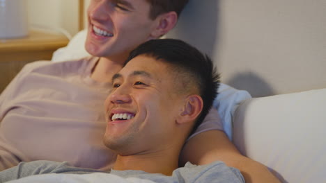 Nahaufnahme-Eines-Liebenden-Gleichgeschlechtlichen-Männlichen-Paares,-Das-Zu-Hause-Im-Bett-Liegt-Und-Gemeinsam-Fernsieht