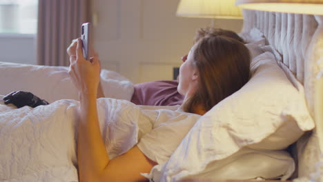 Couple-With-Woman-With-Prosthetic-Arm-In-Bed-Looking-At-Mobile-Phone-Together